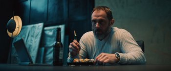 Movie still from “Riders of Justice” (2020), directed by Anders Thomas Jensen – A man sitting at a table with a plate of food in front of him; Medium shot, Low angle