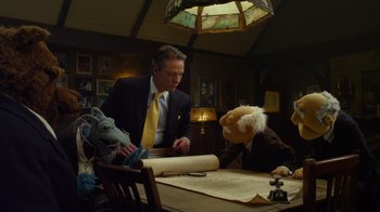 Movie still from “The Muppets” (2011), directed by James Bobin – A man sitting at a table next to two puppets; Medium shot, Low angle