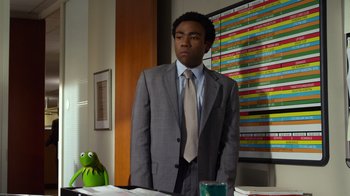 Movie still from “The Muppets” (2011), directed by James Bobin – A man in a suit and tie standing in front of a table; Medium shot, Over the shoulder angle