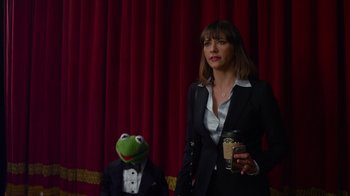 Movie still from “The Muppets” (2011), directed by James Bobin – A woman in a suit holding a drink next to a man in a suit holding a frog mask; Medium shot, Over the shoulder angle