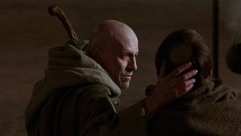 Movie still from “The Name of the Rose” (1986), directed by Jean-Jacques Annaud – An old man with a stick in his hand and a bald head; Close Up shot, Over the shoulder angle