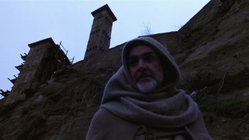 Movie still from “The Name of the Rose” (1986), directed by Jean-Jacques Annaud – A man in a hooded cloak standing in front of a stone wall; Medium shot, Low angle