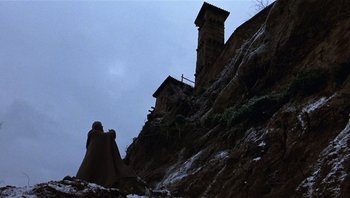 Movie still from “The Name of the Rose” (1986), directed by Jean-Jacques Annaud – A person standing on a hill near a building; Extreme Wide shot, Low angle