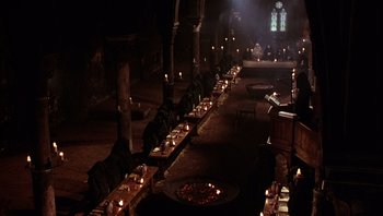 Movie still from “The Name of the Rose” (1986), directed by Jean-Jacques Annaud – A group of people sitting at a table with candles on it; Extreme Wide shot, High angle