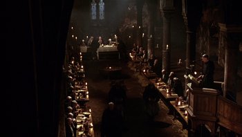 Movie still from “The Name of the Rose” (1986), directed by Jean-Jacques Annaud – A group of people sitting around a table with lit candles; Extreme Wide shot, High angle