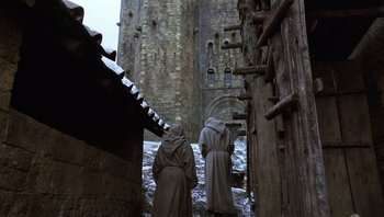 Movie still from “The Name of the Rose” (1986), directed by Jean-Jacques Annaud – Two monks are standing in front of an old castle; Wide shot, Low angle