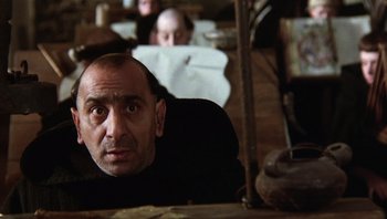 Movie still from “The Name of the Rose” (1986), directed by Jean-Jacques Annaud – A person sitting in front of another person; Close Up shot, Over the shoulder angle