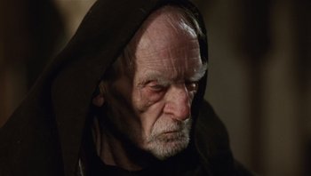 Movie still from “The Name of the Rose” (1986), directed by Jean-Jacques Annaud – An old man wearing a black robe and a black hood; Close Up shot, Low angle