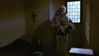 Movie still from “The Name of the Rose” (1986), directed by Jean-Jacques Annaud – An old man wearing a robe and headphones in front of a window; Medium shot, High angle