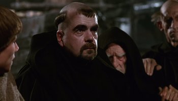 Movie still from “The Name of the Rose” (1986), directed by Jean-Jacques Annaud – A man with a bald head wearing a black robe; Close Up shot, Low angle