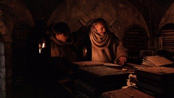 Movie still from “The Name of the Rose” (1986), directed by Jean-Jacques Annaud – Two men in robes are standing in front of a table; Medium shot, Low angle