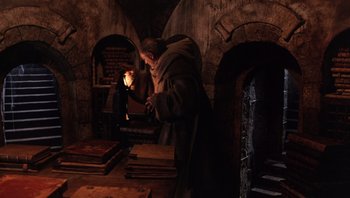 Movie still from “The Name of the Rose” (1986), directed by Jean-Jacques Annaud – A man standing in front of stacks of books; Wide shot, High angle