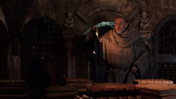 Movie still from “The Name of the Rose” (1986), directed by Jean-Jacques Annaud – A man in a monk's robe lighting a candle in an old building; Medium shot, Low angle