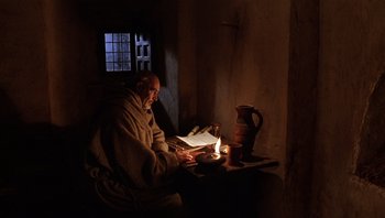 Movie still from “The Name of the Rose” (1986), directed by Jean-Jacques Annaud – An old man sitting in a dark room by a candle; Wide shot, High angle