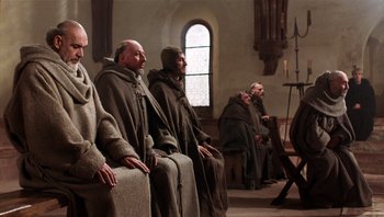 Movie still from “The Name of the Rose” (1986), directed by Jean-Jacques Annaud – A group of monks sitting in a row in front of a window; Wide shot, Low angle