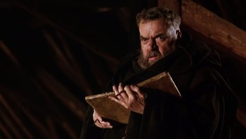 Movie still from “The Name of the Rose” (1986), directed by Jean-Jacques Annaud – A man with a beard holding a book in his hands; Medium shot, Low angle