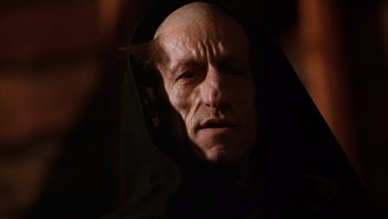 Movie still from “The Name of the Rose” (1986), directed by Jean-Jacques Annaud – An old man wearing a black robe and a black hood; Close Up shot, Low angle