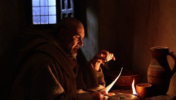 Movie still from “The Name of the Rose” (1986), directed by Jean-Jacques Annaud – A man sitting in front of a lit candle in a room; Medium shot, Low angle