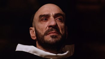 Movie still from “The Name of the Rose” (1986), directed by Jean-Jacques Annaud – A bald man with a beard and a white collar; Close Up shot, Low angle