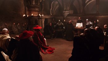 Movie still from “The Name of the Rose” (1986), directed by Jean-Jacques Annaud – A group of people dressed in medieval garb in a room; Wide shot, High angle