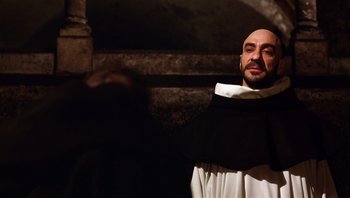 Movie still from “The Name of the Rose” (1986), directed by Jean-Jacques Annaud – A man wearing a black and white robe and standing in front of a stone wall; Close Up shot, Low angle