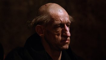 Movie still from “The Name of the Rose” (1986), directed by Jean-Jacques Annaud – An old man with a bald head and a black shirt; Close Up shot, Low angle