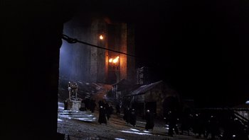 Movie still from “The Name of the Rose” (1986), directed by Jean-Jacques Annaud – A group of people walking in the snow near a building; Extreme Wide shot, High angle