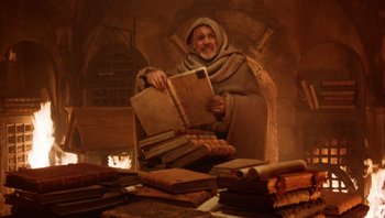 Movie still from “The Name of the Rose” (1986), directed by Jean-Jacques Annaud – An old man sitting in a chair reading a book; Medium shot, High angle