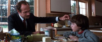 Movie still from “The NeverEnding Story” (1984), directed by Wolfgang Petersen – A man in a black suit is reaching for food from a child; Medium shot, Over the shoulder angle