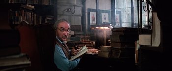 Movie still from “The NeverEnding Story” (1984), directed by Wolfgang Petersen – An older man sitting at a table with a book; Medium shot, Low angle
