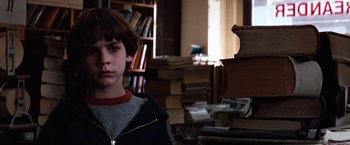 Movie still from “The NeverEnding Story” (1984), directed by Wolfgang Petersen – A young boy standing next to a pile of books; Close Up shot, Over the shoulder angle