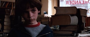 Movie still from “The NeverEnding Story” (1984), directed by Wolfgang Petersen – A young boy is standing in front of a stack of books; Close Up shot, Over the shoulder angle