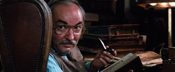 Movie still from “The NeverEnding Story” (1984), directed by Wolfgang Petersen – An older man holding a pen in his hand; Close Up shot, Low angle