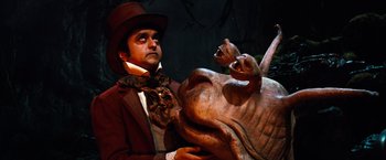Movie still from “The NeverEnding Story” (1984), directed by Wolfgang Petersen – A man in a top hat and a brown jacket holding a brown animal; Medium shot, High angle