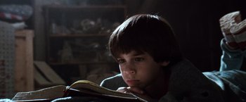 Movie still from “The NeverEnding Story” (1984), directed by Wolfgang Petersen – A young boy is reading a book in a dark room; Close Up shot, Low angle
