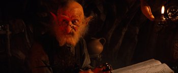 Movie still from “The NeverEnding Story” (1984), directed by Wolfgang Petersen – An old man with a beard and glasses is holding a pen; Close Up shot, Low angle