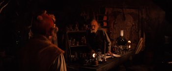 Movie still from “The NeverEnding Story” (1984), directed by Wolfgang Petersen – An old man standing in a room next to a table; Medium shot, Over the shoulder angle