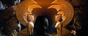 Movie still from “The NeverEnding Story” (1984), directed by Wolfgang Petersen – A woman is looking at a pair of statues of gargoyles; Wide shot, Low angle