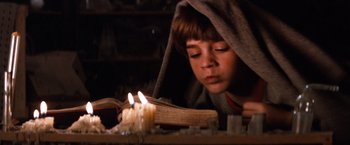 Movie still from “The NeverEnding Story” (1984), directed by Wolfgang Petersen – A young boy lighting a candle on top of an open book; Medium shot, High angle