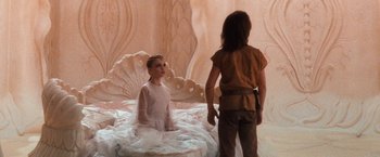 Movie still from “The NeverEnding Story” (1984), directed by Wolfgang Petersen – A young girl sitting on top of a bed next to a young man; Medium shot, Over the shoulder angle