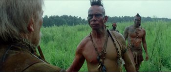 Movie still from “The New World” (2005), directed by Terrence Malick – A man with a beard and a necklace is standing in the grass; Close Up shot, Low angle