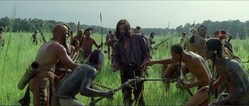 Movie still from “The New World” (2005), directed by Terrence Malick – A group of people in a field with a man holding a bow and arrow; Wide shot, Over the shoulder angle