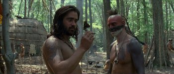 Movie still from “The New World” (2005), directed by Terrence Malick – A man with long hair and tattoos on his face and a man with long hair and tattoos on his face; Medium shot, Over the shoulder angle