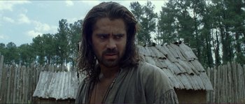 Movie still from “The New World” (2005), directed by Terrence Malick – A man with long hair and a beard is standing in front of a wooden hut; Close Up shot, Over the shoulder angle