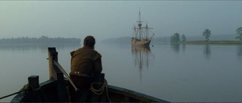 Movie still from “The New World” (2005), directed by Terrence Malick – A man sitting on the back of a boat looking at a boat in a body of water; Extreme Wide shot, Over the shoulder angle