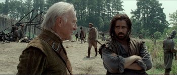 Movie still from “The New World” (2005), directed by Terrence Malick – Two men standing next to each other on a dirt field; Medium shot, Over the shoulder angle