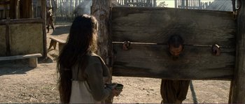 Movie still from “The New World” (2005), directed by Terrence Malick – A woman standing next to a wooden structure; Medium shot, Over the shoulder angle