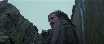 Movie still from “The New World” (2005), directed by Terrence Malick – A man with long hair is standing in front of a stone wall; Medium shot, Low angle