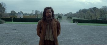 Movie still from “The New World” (2005), directed by Terrence Malick – A man with long hair standing on a brick road; Medium shot, Over the shoulder angle