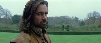 Movie still from “The New World” (2005), directed by Terrence Malick – A man with long hair and a beard is standing in a field; Close Up shot, Over the shoulder angle